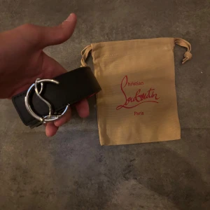 Svart bälte från Christian Louboutin med silverfärgat spänne - Säljer ett svart bälte från Christian Louboutin med ett unikt, silverfärgat spänne. Bältet har en röd insida som ger en snygg kontrast. Kommer med originalpåse från märket.