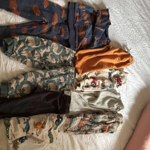 Färgglada mjukisbyxor med djurmotiv - Säljer ett gäng mjukisbyxor i olika färger och mönster, bland annat blå med björnar, gröna med dinosaurier, orange, beige med traktorer och flerfärgade med bilar och djur. Perfekta för chill dagar och lek, mjuka muddar och elastisk midja. Har även matchande tröjor till byxorna på bilden 