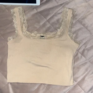 Beige ribbad linnetopp med spets Shein - Supersöt beige ribbad linnetopp från Shein med breda axelband och fina spetsdetaljer längs kanterna. Toppen är croppad och har en mjuk, stretchig känsla som gör den perfekt till jeans eller kjol. Enkel att styla för en trendig look.