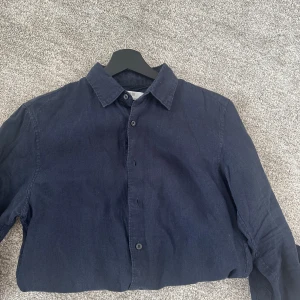 Mörkblå linneskjorta från Uniqlo - Säljer en stilren mörkblå skjorta i linne från Uniqlo. Skjortan har klassisk krage, knäppning framtill och långa ärmar. Användts sparsamt och är i bra skick. Nypris 600 mitt pris 249. Kontakta vid frågor. 