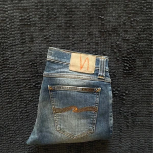 Blå jeans från Nudie Jeans, stl 29/32 - Säljer ett par klassiska blå jeans från Nudie Jeans. Modellen har normal passform och raka ben, med ikonisk broderad bakficka och läderpatch i midjan. Perfekta till sneakers och hoodie.