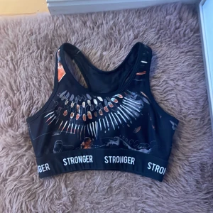 Svart sport-bh från Stronger med mönster - Cool svart sport-bh från Stronger med färgglatt abstrakt mönster och bred resår med logga. Perfekt för träning och har brottarrygg för extra stöd. Använd fåtal gånger och är i mycket bra skick. Hör av dig om du har frågor eller funderingar💕