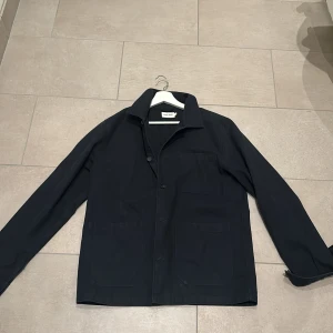 Mörkblå overshirt från East West - Snygg mörkblå overshirt från East West med klassisk krage och knäppning framtill. Ny pris 999kr men den är använd en vår så därför säljer jag den billigt