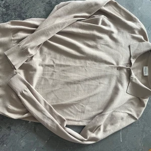 Beige pikétröja från John Henric - Säljer en stilren beige pikétröja från John Henric i storlek M. Tröjan har långa ärmar, klassisk krage och knäppning vid halsen. Perfekt för en avslappnad men ändå uppklädd look.