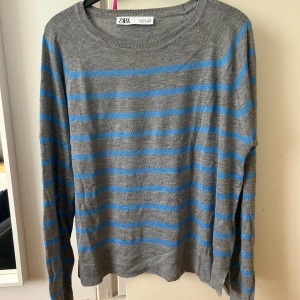 Grå och blå randig tröja från Zara - Säljer en grå långärmad tröja från Zara med blåa horisontella ränder. Tröjan har rund halsringning och är tillverkad i ett mjukt material som passar perfekt till vardags. Enkel och stilren design.