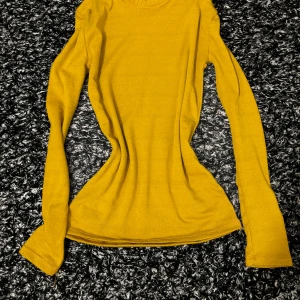 Gul långärmad stickad tröja - Säljer en snygg gul stickad tröja med lång ärm och rund halsringning. Perfekt för lager-på-lager och passar till både jeans och kjol. Enkel och stilren design som är lätt att matcha. Passar kroppen