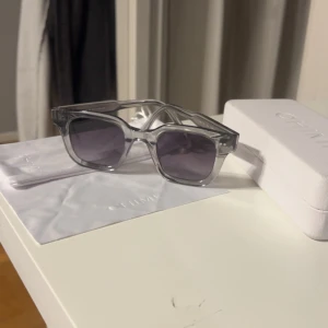 Grå transparenta solglasögon från CHIMI - Snygga solglasögon från CHIMI i transparent grå plast med mörka glas. Rektangulär form och stilren design, perfekt för dig som vill ha en modern accessoar. Levereras med originalfodral och putsduk.