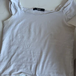 Vit topp från Bik Bok - Säljer en enkel vit topp från Bik Bok med breda axelband och rak passform. Toppen är ärmlös och har en mjuk bomullskänsla, perfekt till sommaren. Snygg att matcha med jeans eller kjol!