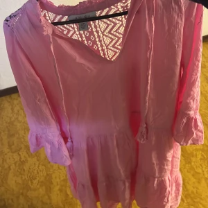 Rosa kortklänning från Amisu - Söt rosa kortklänning från Amisu med volangdetaljer och knytband vid halsen. Klänningen har trekvartsärmar och spetsmönster upptill på ryggen. Lätt och luftig modell, perfekt för varma dagar.