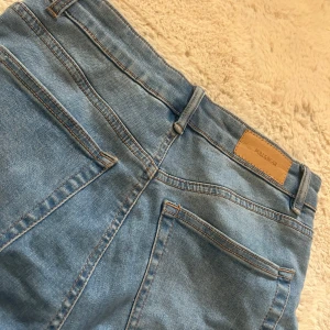 Blå wide jeans från Pull&Bear - Säljer ett par ljusblå jeans från Pull&Bear i storlek 38. Jeansen har hög midja, raka breda ben och klassiska bakfickor. Tillverkade i jeansmaterial med snygga kontrastsömmar och bälteshällor.