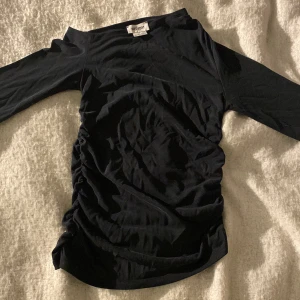 Svart topp med rynkade sidor Weekday XS - Svart långärmad of-shoulder topp från Weekday i storlek XS. Modellen har rynkade sidor som ger en snygg och trendig look. Tunt och mjukt material, perfekt att styla med jeans eller kjol. Enkel och stilren design med rund halsringning.