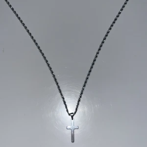 Silverfärgat halsband med kors - Stilrent halsband i silverfärg med tvinnad kedja och ett enkelt kors som hänge. Kedjan är i bra skick och inte används så mycket, skickar varan samma dag och är inte sugen på pruta