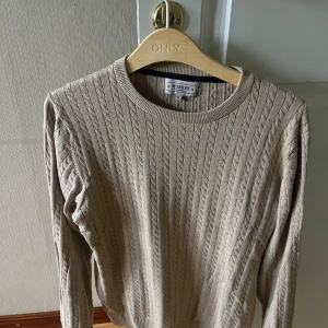 Beige kabelstickad tröja från Murrey - Snygg beige kabelstickad tröja från Murrey med rund halsringning och långa ärmar. Perfekt för lager-på-lager och passar till både jeans och kjol. Mjuk och skön känsla tack vare bomullsmaterialet.
