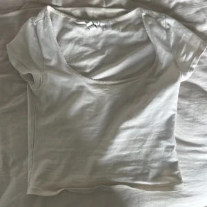 Vit kortärmad topp från Divided - Säljer en enkel och stilren vit topp från Divided. Toppen har korta ärmar och en rund, djup ringning. Perfekt att matcha med jeans eller kjol för en clean look.