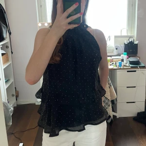 Svart glittrig topp från Neo Noir - Snygg svart topp från Neo Noir med små vita stenar och volangdetaljer. Helt oanvänd och säljer då den inte passade. Skriv för fler bilder