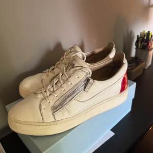 Vita sneakers från Giuseppe Zanotti -  vita sneakers i skinn från Giuseppe Zanotti med röda detaljer på hälen, silverfärgade dragkedjor på sidorna och den ikoniska loggan där fram. Det 43 men passar även 44, det är i bra skick inga större defekter. Fråga vid funderingar. Pris ej hugget i sten🤝