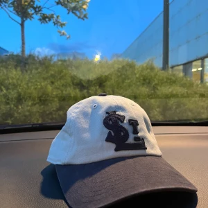 Beige och svart keps med broderad logga NY - Snygg keps i beige med svart skärm och broderad logga framtill. Köpt för en vecka sedan använd en gång. 