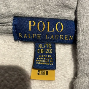 Grå  zip hoodie från Ralph Lauren - Säljer en stilren grå hoodie från Ralph Lauren med dragkedja och huva. Den har en liten broderad logga på bröstet och är perfekt för en avslappnad look. Passar bra till både jeans och joggers. Nypris 1600 passar stl S och M , xl är barn storleken