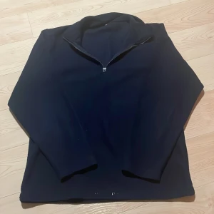 Fleece tröja med dragkedja - Säljer en mörkblå fleece tröja med halv dragkedja. Perfekt för kyliga dagar med sin mjuka och varma känsla. Tröjan har långa ärmar och en hög krage för extra värme. Passar bra till både vardag och utomhusaktiviteter. S/M