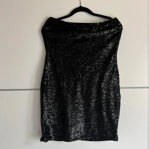 Svart paljettkjol från Bisser - Snygg svart kjol från Bisser täckt med glittrande paljetter. Perfekt för att sticka ut på festen. Kjolen har en tight passform och är knälång. Den är tillverkad i ett mjukt material som känns bekvämt mot huden.