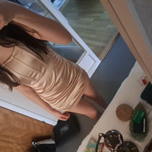 Champagnefärgad klänning - Snygg champagnefärgad kortklänning med tight passform. Klänningen har en stilren design med axelbandslös stil och är perfekt för festliga tillfällen. Materialet ser ut att vara glansigt och elegant.