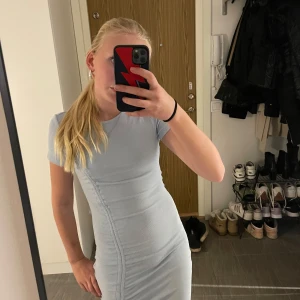 Ljusblå klänning från Divided - Säljer en ljusblå klänning från Divided med korta ärmar och en snygg rynkad detalj på sidan. Klänningen har en tight passform och är perfekt för en stilren look. Den är gjord i ett mjukt och bekvämt material. Perfekt en varm sommardag när man vill vara lite uppklädd. 🫐