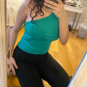 Grön oneshoulder topp från Stories - Säljer en snygg grön oneshoulder topp från Stories. Toppen är ribbad och har en tight passform som framhäver figuren. Perfekt för att ge en stilren look. Aldrig använt. Hör av dig vid intresse! 💚