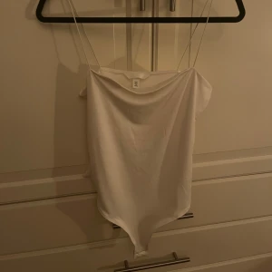 Vit axelbandslös topp - Säljer en stilren vit axelbandslös topp med smala axelband. Perfekt för varma sommardagar eller som ett basplagg i garderoben. Enkel och elegant design som passar till många olika outfits.