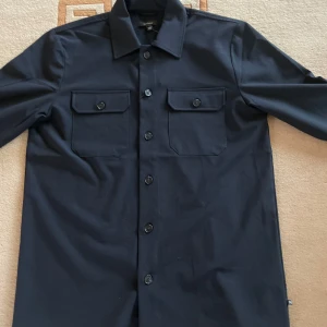 Mörkblå overshirt från Matinique - Snygg mörkblå overshirt från Matinique med knappar framtill och två bröstfickor med lock. Perfekt för lager-på-lager stil. Passar bra till både casual och mer uppklädda tillfällen. Ny pris 1300kr!Säljer för att tröjan var  för stor och kommer inte lämna tillbaka!