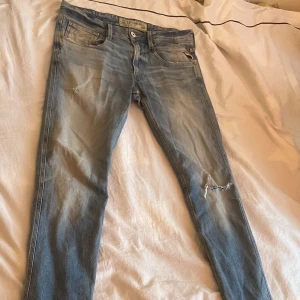 Blå jeans från Replay - Säljer ett par snygga blå jeans från Replay, modell Anbass. De har en klassisk femficksdesign med slitna detaljer och en dragkedja. Perfekta för en avslappnad stil. Waist 31 & length 34