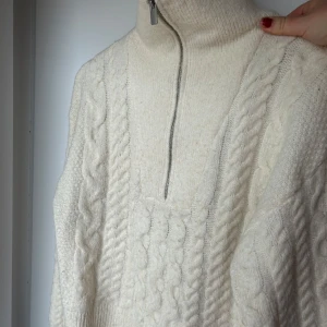 Vit stickad tröja från BikBok - Mysig krämfärgad stickad tröja från BikBok med kabelstickat mönster och dragkedja vid halsen. Perfekt för kyliga dagar med sin höga krage och långa ärmar. En klassisk och stilren design som passar till det mesta. Inte använt så mycket eftersom den är för liten för mig :(