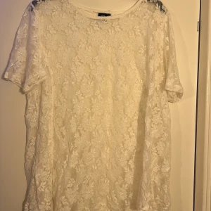 Vit spetsblus från Cotonel - Säljer en elegant vit spetsblus från Cotonel. Blusen har korta ärmar och ett vackert blommigt mönster. Perfekt för att ge en romantisk touch till din outfit. 💫