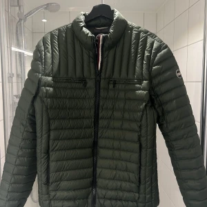 Grön jacka från Colmar - Snygg grön quiltad jacka från Colmar med dragkedja framtill. Jackan har en stilren design med två dragkedjefickor på bröstet och en hög krage. Perfekt för kyligare dagar.