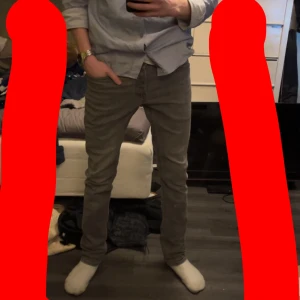 Grå slim jeans från Jack & Jones - Snygga grå slim fit jeans från Jack & Jones, modell Glenn. Perfekta för en stilren look med klassisk design och knappgylf. Passar bra till både skjorta och t-shirt.