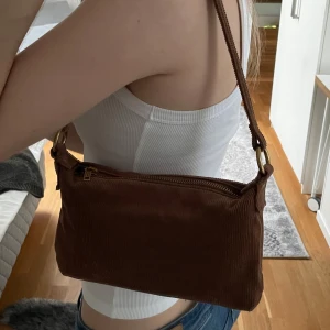 Brun axelväska - Säljer denna super fina  bruna axelväskan från Brandy Melville. Är i manchester med en guldig dragkedja. Passat till så mycket och är en praktisk storlek. Nästan aldrig använd, hör av er om frågor. 