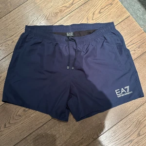 Mörkblå badbyxor från EA7 Emporio Armani - Snygga mörkblå badbyxor från EA7 Emporio Armani med elastisk midja och snörning.