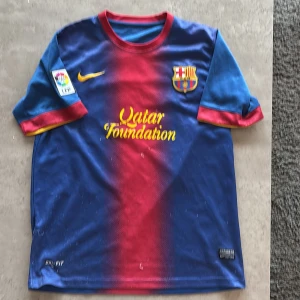 Blå och röd fotbollströja från Nike - Säljer en klassisk FC Barcelona fotbollströja från Nike med Messi 10 på ryggen. Tröjan är blå och röd med gula detaljer och har korta ärmar. Perfekt för alla Barca-fans! 🏆