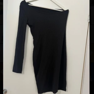 Klänning  - Snygg svart ribbad klänning med en lång ärm och offshoulder-design. Endast testad.