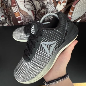 Svartvita träningsskor från Reebok - Snygga svartvita träningsskor från Reebok med Crossfit-logga. Skorna har ett mönstrat tyg och snörning för en säker passform. Perfekta för intensiva träningspass.