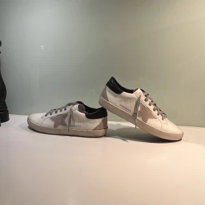 Vita sneakers med stjärndetalj - Snygga vita sneakers med en grå stjärna på sidan och svarta detaljer vid hälen. Skorna har grå snörning och en klassisk design som passar perfekt för en avslappnad stil. Skorna är använda endast två gånger! Pris kan diskuteras och vid andra funderingar är det bara att höra av sig!