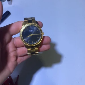 Guldfärgad klocka från Regal - Elegant guldfärgad klocka från Regal med svart urtavla. Klockan har en stilren design med guldfärgade visare och markeringar. Armbandet är i metall och justerbart med extra länkar inkluderade. Perfekt för den som vill ha en tidlös accessoar. Ny pris 500.