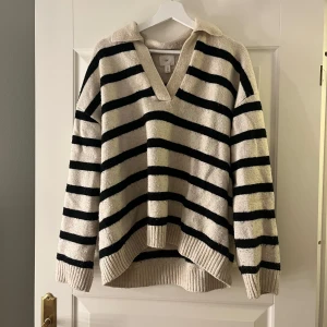 Randig stickad tröja från H&M - Säljer en mysig stickad tröja från H&M i beige och svart med randigt mönster. Tröjan har en v-ringad krage och långa ärmar, perfekt för kyligare dagar. Den har en avslappnad passform och ribbade kanter.