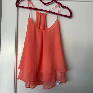 Korallfärgad linnetopp från Bershka - Säljer en snygg korallfärgad linnetopp från Bershka. Toppen har tunna axelband och ett dubbelt lager tyg som ger en fin volangeffekt. Perfekt för varma sommardagar! 🌞använd 1 gång.