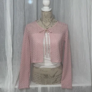 Rosa spetskofta och vit tubtopp - Säljer en set som består av en söt rosa spetskofta med knytband framtill och en vit ribbad tubtopp. Koftan är croppad och har långa ärmar, perfekt för lager-på-lager-stil. Tubtoppen är enkel och stilren, idealisk för sommardagar. Från Shein, nyskick. Kan säljas separat då det blir 30kr för varje plagg.