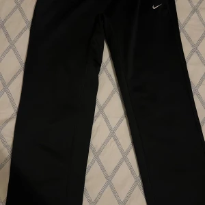 Svarta träningsbyxor från Nike - Säljer ett par vida svarta träningsbyxor från Nike med Dri-FIT-teknologi. Byxorna har en elastisk midja och en liten Nike-logga på framsidan. Perfekta för träning och sportaktiviteter. Storlek S. Pris kan diskuteras. 