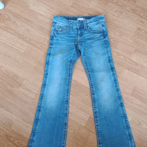 Blå bootcut jeans - Snygga blå bootcut jeans med klassisk femficksdesign och knappar på bakfickorna. Perfekta för en avslappnad stil med en touch av retro. De har en bekväm passform och är tillverkade i ett slitstarkt denimtyg.