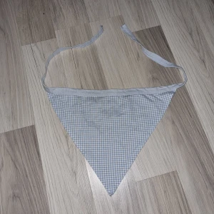 Rutig bandana  - Bandana med rutigt mönster i ljusblått och vitt. Den har knytband i sidorna för justerbar passform. Passar barn i förskolan