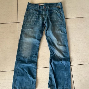 Blå jeans från Replay och Ralf Lauren - Snygga blå jeans från Replay och Ralf Lauren med en klassisk design. De har en rak passform och är tillverkade i slitstarkt denim. Byxorna har fem fickor och en knappgylf med dragkedja. Perfekta för en avslappnad stil. Storlek W36 L34