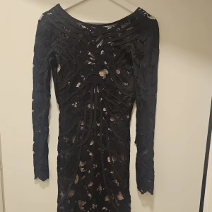 Svart elegant klänning - Snygg svart klänning med spets detaljer och långärmad design. Perfekt för en kväll ute med vänner. Den har en tight passform som framhäver figuren. Otroligt elegant lång klänning i svart spets i strl XS, endast provad. Öppen rygg.