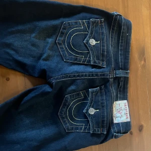 Mörkblå jeans från True Religion - Snygga mörkblå jeans från True Religion med låg midja och klassiska femficksdesign. De har dekorativa sömmar på bakfickorna och silverfärgade knappar. Perfekta för en avslappnad stil.